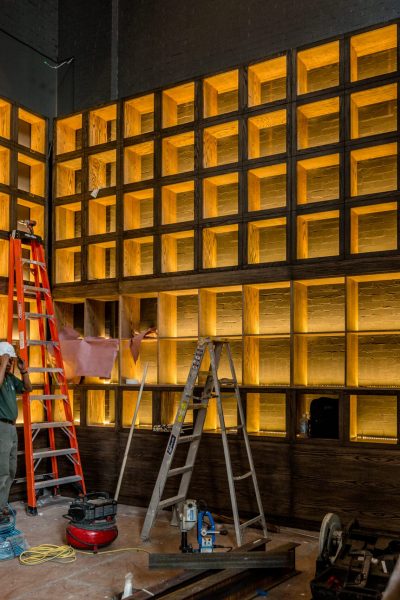 Illuminated wood grid feature wall under construction with ladders and tools